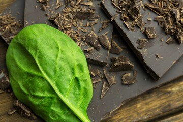 Showing green spinach leaf resting diagonally on dark chocolate pieces and shavings on wooden board