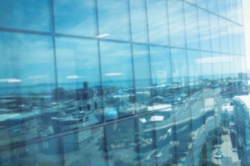 Defocussed image of modern cityscape and blue sky reflected in glass building, with copy space