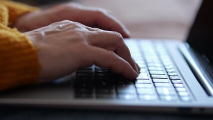 Elderly woman typing on laptop keyboard at home - Powered by Adobe