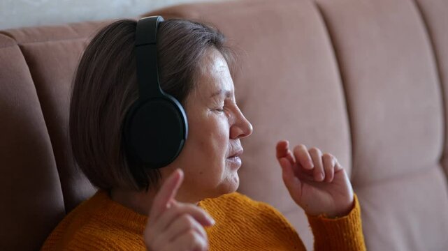 Elderly woman enjoying music with headphones on sofa