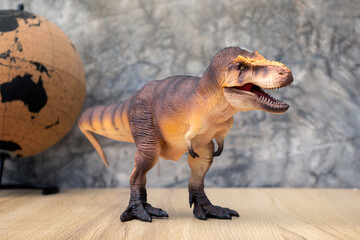 T-rex Dinosaur toy. Tyrannosaurus rex with mini globe on wooden table and dark background bare...