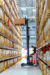 forklift operates inside a clean and organized warehouse, lifting a pallet between tall racks of cardboard boxes.