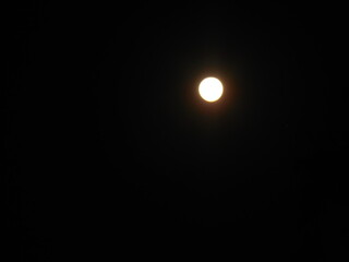 Bright full moon shining in the dark night sky, surrounded by a soft glowing halo. Minimalist celestial night photography