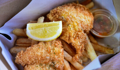 Classic Traditional English or British culinary delight Fish and Chips, golden deep fried fish with Lemon wedges in a paper box for takeaway as Lunch Box