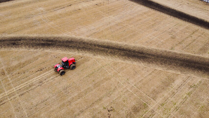 Areal view of red tractor on harvested farm field