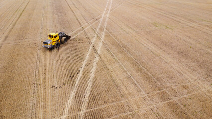 Areal view of yellow tractor on harvested farm field