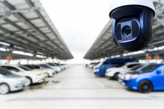 Fototapeta CCTV surveillance camera monitoring modern car parking lot with many parked vehicles under solar panel roof