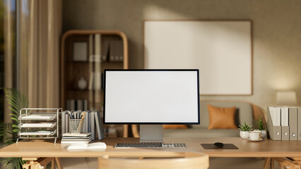 White screen computer with books and stationary on wooden table in a cosy living room or study room.