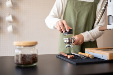 Close up of green apron barista taking out used coffee grounds cleaning machine at cafe counter bar.