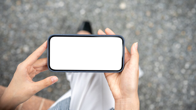 Close up of hands holding white screen smartphone horizontally watching or playing sitting on bench.