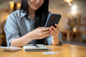 Close up of woman hands holding phone watching video or texting over notebook on cafe wooden table.