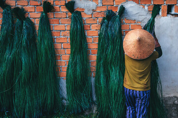 Vietnamese woman in traditional straw hat dries dyed reeds at woven mat factory in village in...
