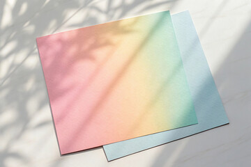Two pastel colored sheets of paper with soft shadows on a white surface