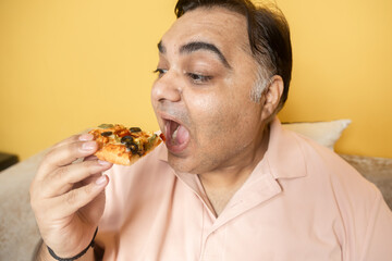 Hungary overweight fat indian man eating cheese pizza. Plus size guy enjoy fatty junk food. Obese male taking a bite of high calorie meal. Obesity and weight gain. Closeup
