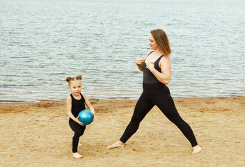 A mother plays ball with her six-year-old daughter on the beach by the lake on a summer day.