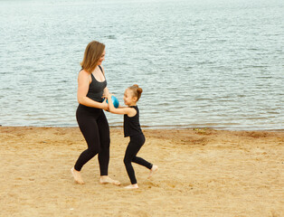 A mother plays ball with her six-year-old daughter on the beach by the lake on a summer day.