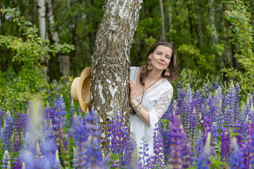 a woman in a straw hat and a white lace dress holding a bouquet of lupines. It stands against the...