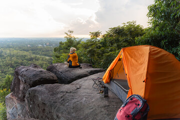 A person is sitting on a rock next to a tent. The tent is orange and has a metal pole