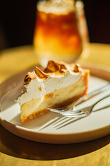 A creamy cheesecake slice sits beside a refreshing iced tea in warm sunlight