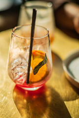 Bright cocktail filled with ice, orange, and mint leaves brings summer vibes to a cozy cafe