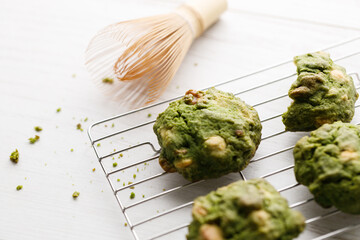 Closeup of fresh baked matcha cookies with Chasen, bamboo whisk, on white wooden background.