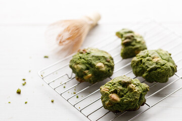 Closeup of fresh baked matcha cookies with Chasen, bamboo whisk, on white wooden background.