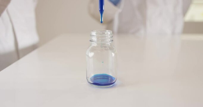 Sample drops of blue ink are poured into a glass by scientists with a pipette in a laboratory