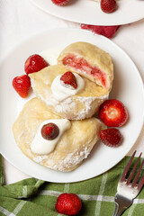 Cut-open strawberry vareniki reveal a juicy, textured filling, garnished with cream and fresh fruit. Great for recipe books and culinary storytelling.