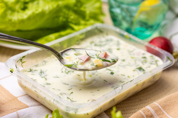 Spoonful of okroshka above a plate. Classic cold summer soup with herbs and veggies