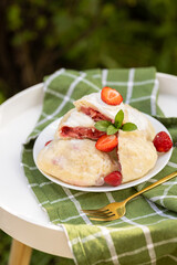 Traditional Ukrainian strawberry dumplings cut open to reveal juicy filling. Served with sour cream and fresh mint on a summer garden table.