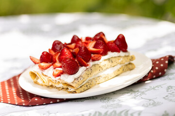 Strawberry crepe cake with whipped cream and poppy seeds served outdoors. Summer picnic with fresh berries and golden light.