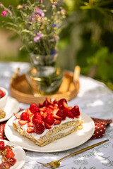 Inviting crepe cake with strawberries and cream. Cozy garden table ready for summer celebration.
