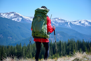 Female hiker with backpack and trekking poles walking in the mountains. Adventure lifestyle in...