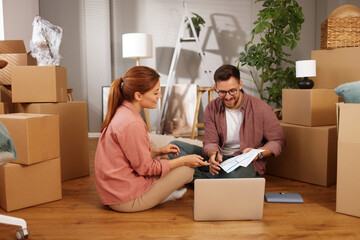 Couple sits on the floor in their new living room filled with packed boxes, discussing moving plans...
