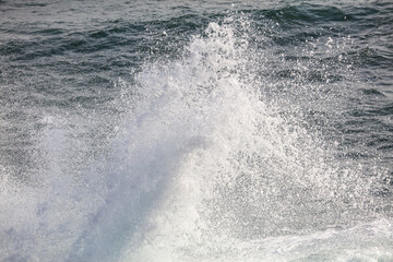 A large wave crashing into the ocean, creating a spray of white foam