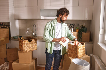 A man sorts through boxes in a newly relocated kitchen, preparing to unpack items while surrounded...
