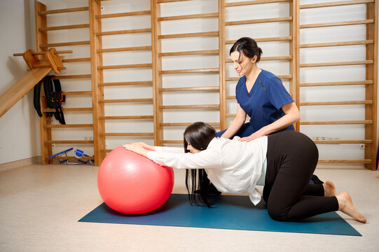 Pregnant woman doing prenatal exercises with physiotherapist using a fitness ball. Female specialist guiding pregnant client in maternity physical therapy session. - Powered by Adobe