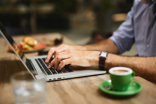A business professional types on a laptop at a cafe, with a steaming cup of coffee and a plate of snacks nearby, showcasing the blend of work and relaxation during a busy day.