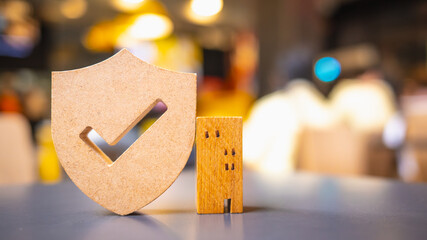 Wooden house model and real estate insurance ideas, and small shield icon. Housing insurance against impending loss and fire, building fire insurance concepts.