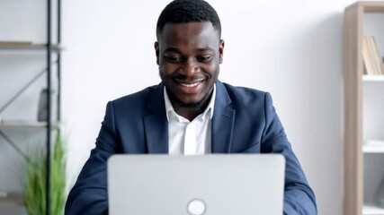 A dark-skinned man in a blue suit working on a laptop in an office setting - Powered by Adobe