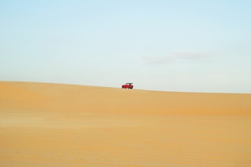 Red Vehicle Driving Across Arid Desert Landscape Under Pale Sky. Mui Ne, Vietnam, White Dunes.