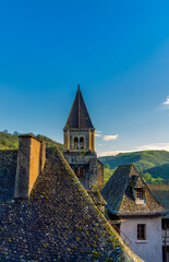 Medieval houses with tiled roofs and the historic tower of the Abbey of Sainte-Foy, in the medieval village of Conques, France, at sunset.