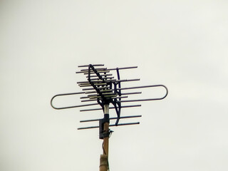 Outdoor metal television antenna mounted on a high wooden pole with wires, isolated on bright clear...