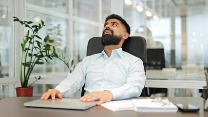 Calm Indian businessman in light shirt closes laptop, leaning back in chair to rest eyes at corporate office desk. Relaxed professional male finds peaceful moment in bright workspace. - Powered by Adobe