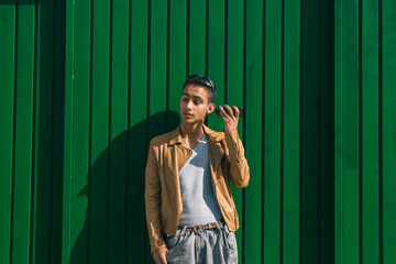 young casual man leaning against green wall with mobile phone listening to audio