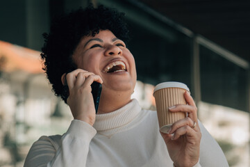 Smiling woman drinking coffee while talking on the phone outside