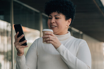 woman taking a break outside the office drinking coffee and looking at her phone