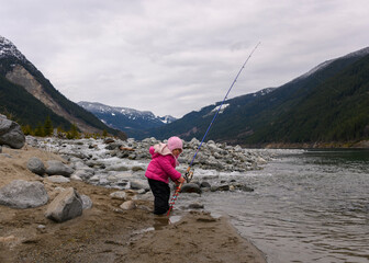 Child fishing by a river in the mountains during a cloudy day in early spring