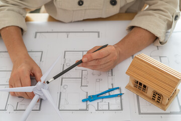 Engineer is designing a sustainable house powered by a wind turbine, using blueprints and a scale...