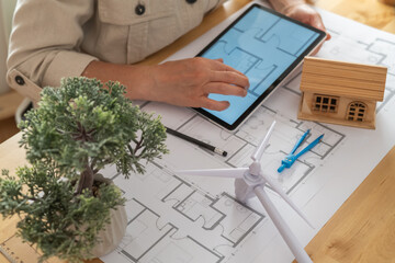 Architect using a digital tablet to design a sustainable and ecological house project with a small wind turbine, promoting renewable energy and green building practices